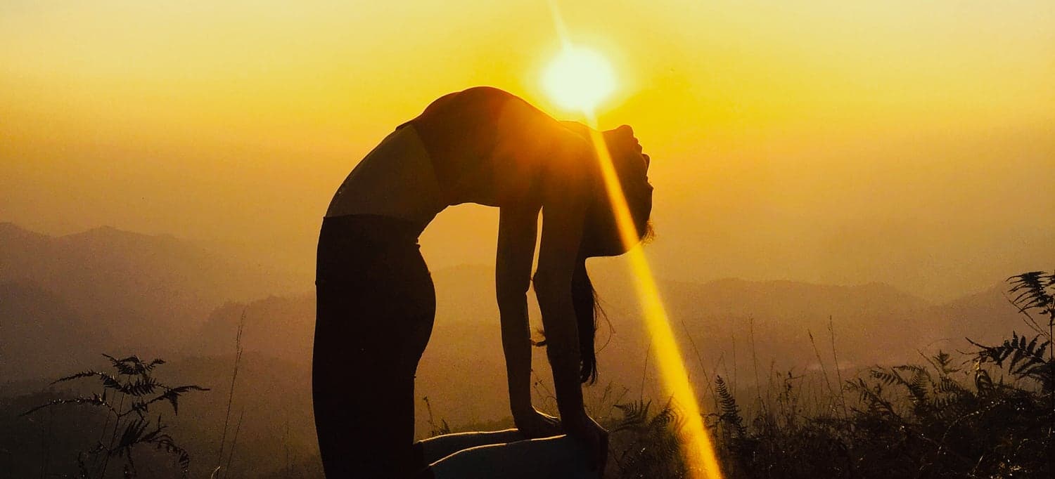 Silhouette of Nicha in wheel pose at sunrise, the sun resting in the arch of her back