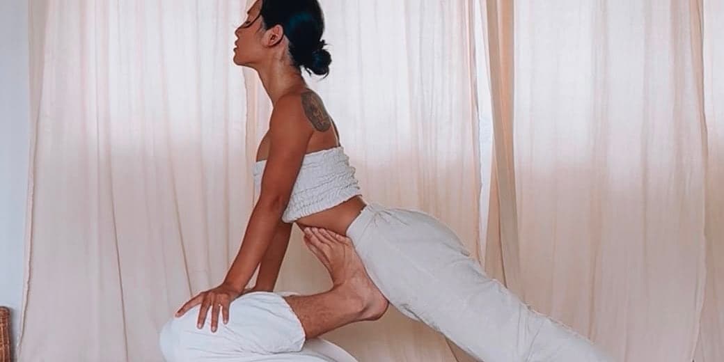 Nicha in a standing lunge, pressing warmth into a client's legs during a Thai Yoga Massage